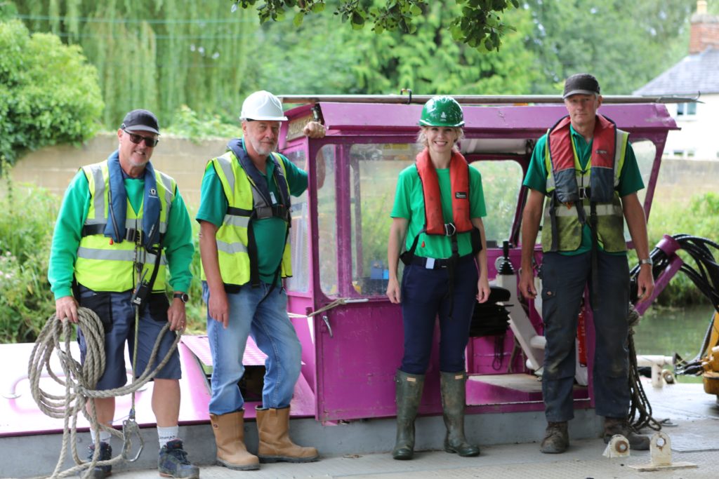Four volunteers stood smiling in front of a purple canal boat.