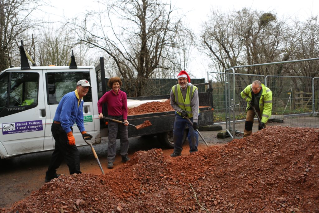 Four volunteers pictured shoveling gravel onto a truck.
